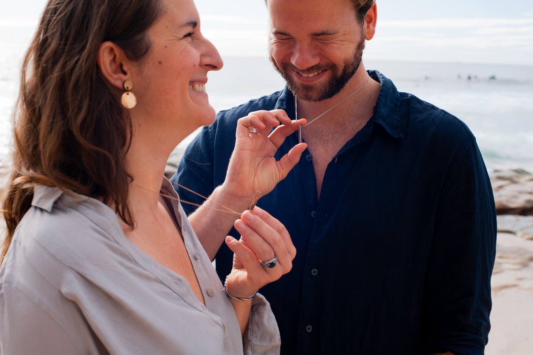 Laughing man and woman in seashore wearing Breathe Into Peace Mindful Breathing Necklace